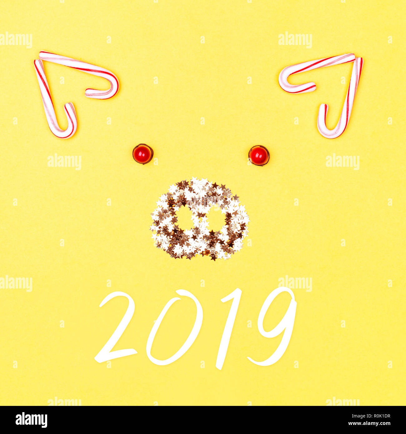 Christmas pig face made of candy cane lollipops and golden confetti on yellow background. Concept of animal 2019. Stock Photo