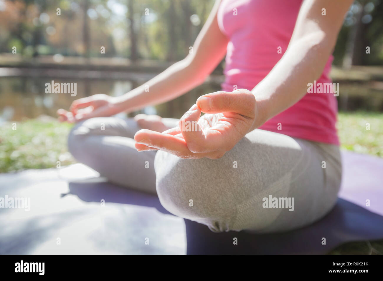 Close up of female hands doing yoga in meditation pose on fitness mat at park. Healthy Lifestyle Workout. Stock Photo