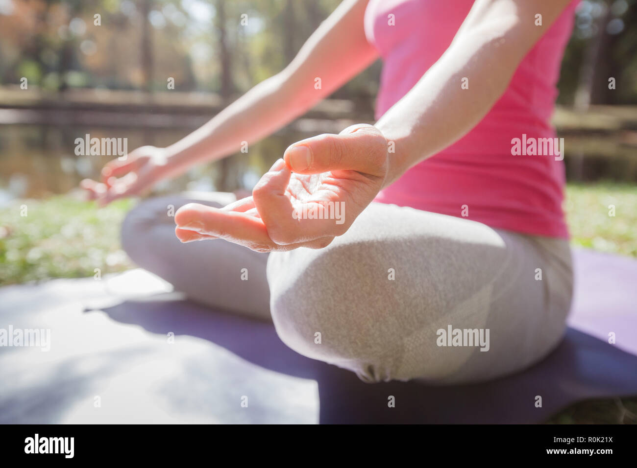 Close up of female hands doing yoga in meditation pose on fitness mat at park. Healthy Lifestyle Workout. Stock Photo