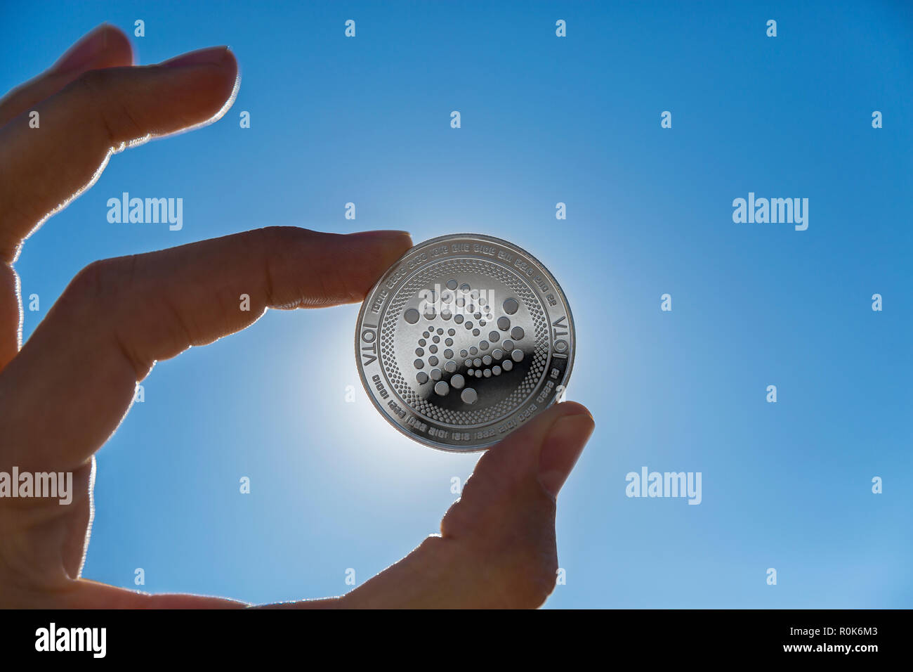Iota cryptocurrency physical coin held between the fingers against the sun  in the blue sky Stock Photo - Alamy