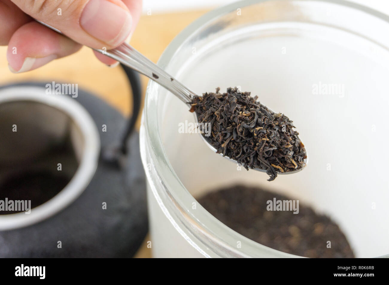 Close-up spoonful of gourmet loose black tea and cast iron tea pot. Beautiful texture. Stock Photo