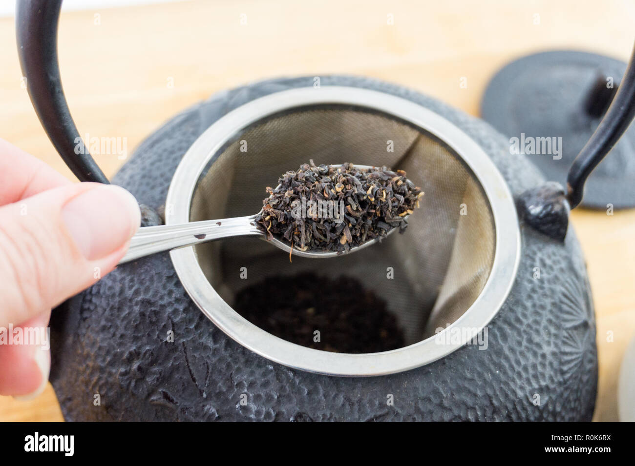 Close-up spoonful of gourmet loose black tea and cast iron tea pot. Beautiful texture. Stock Photo