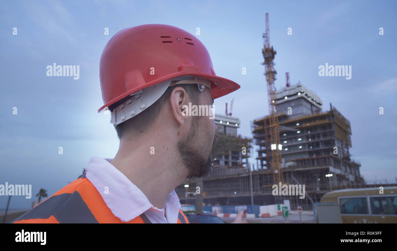 Man in a helmet, architect, engineer, manager tells about the progress of construction in evening Stock Photo
