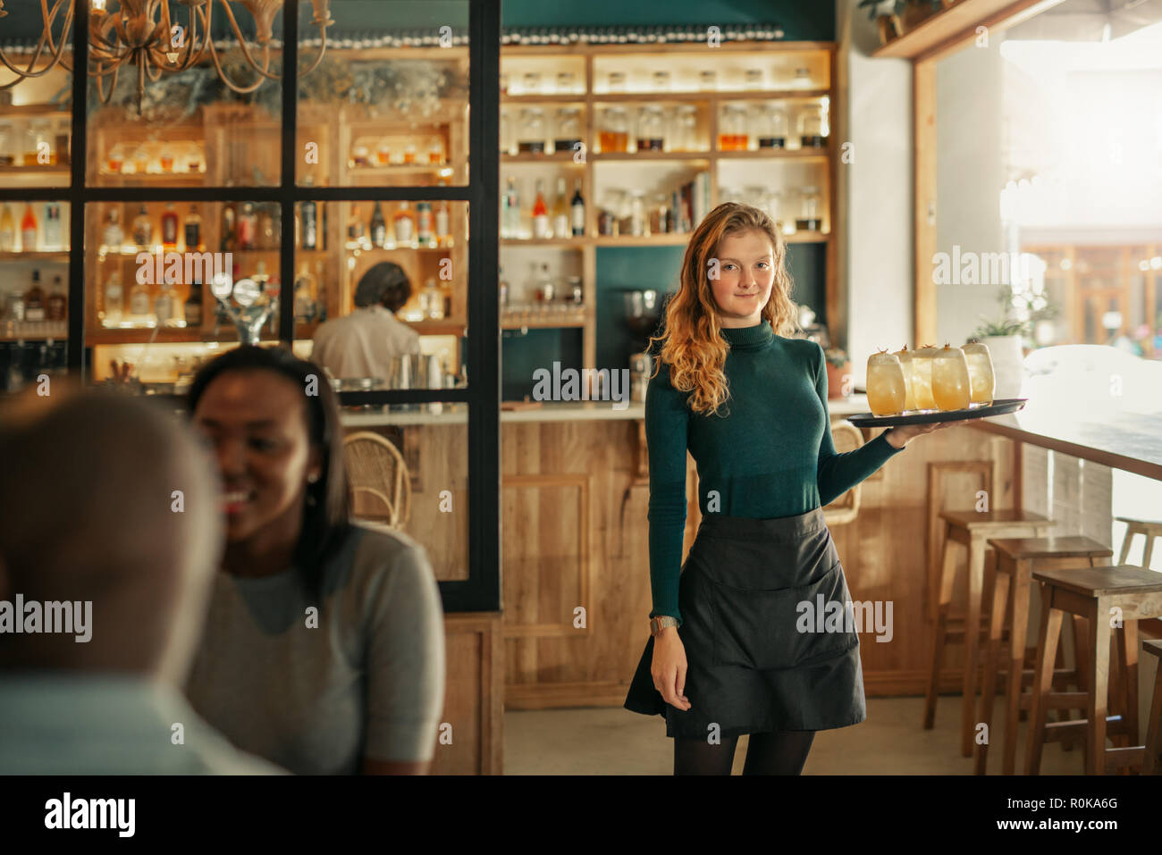 Smiling bar waitress standing with a tray of drinks Stock Photo