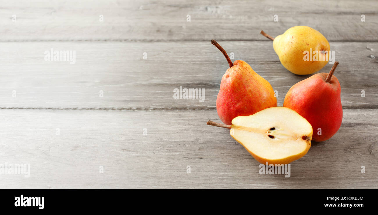 Three whole ripe red and yellow pears, and one cut in half on gray wood boards. Banner size with place for text on the left. Stock Photo