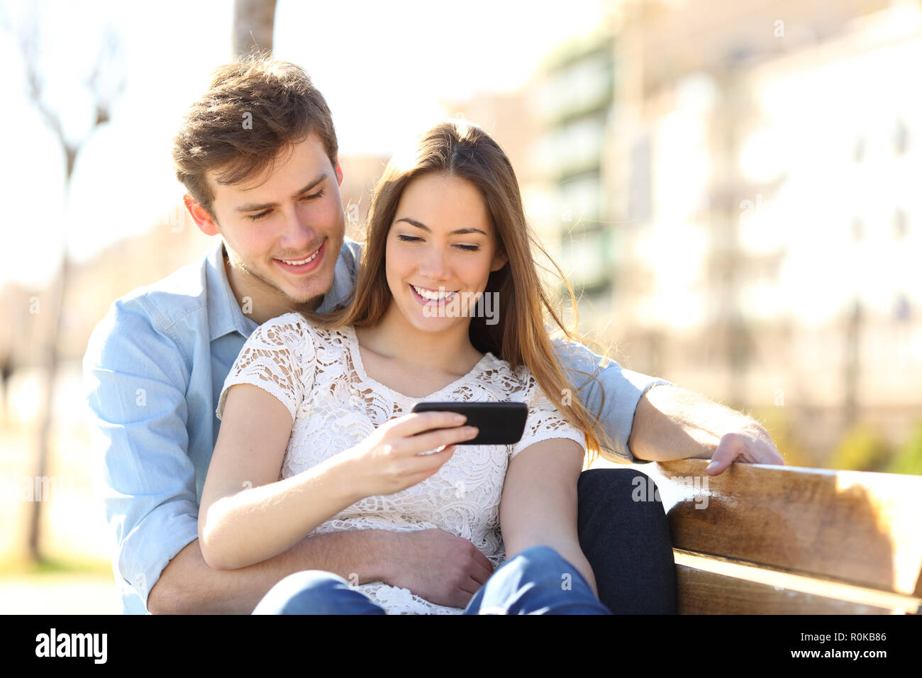 Happy couple listening to music together sitting on a bench in a park Stock Photo