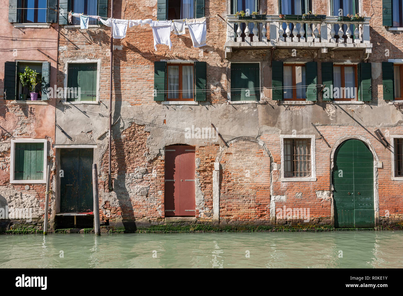 Old brick buildings and painted green shutters with white washing hanging out to dry on a canal Venice Italy Stock Photo