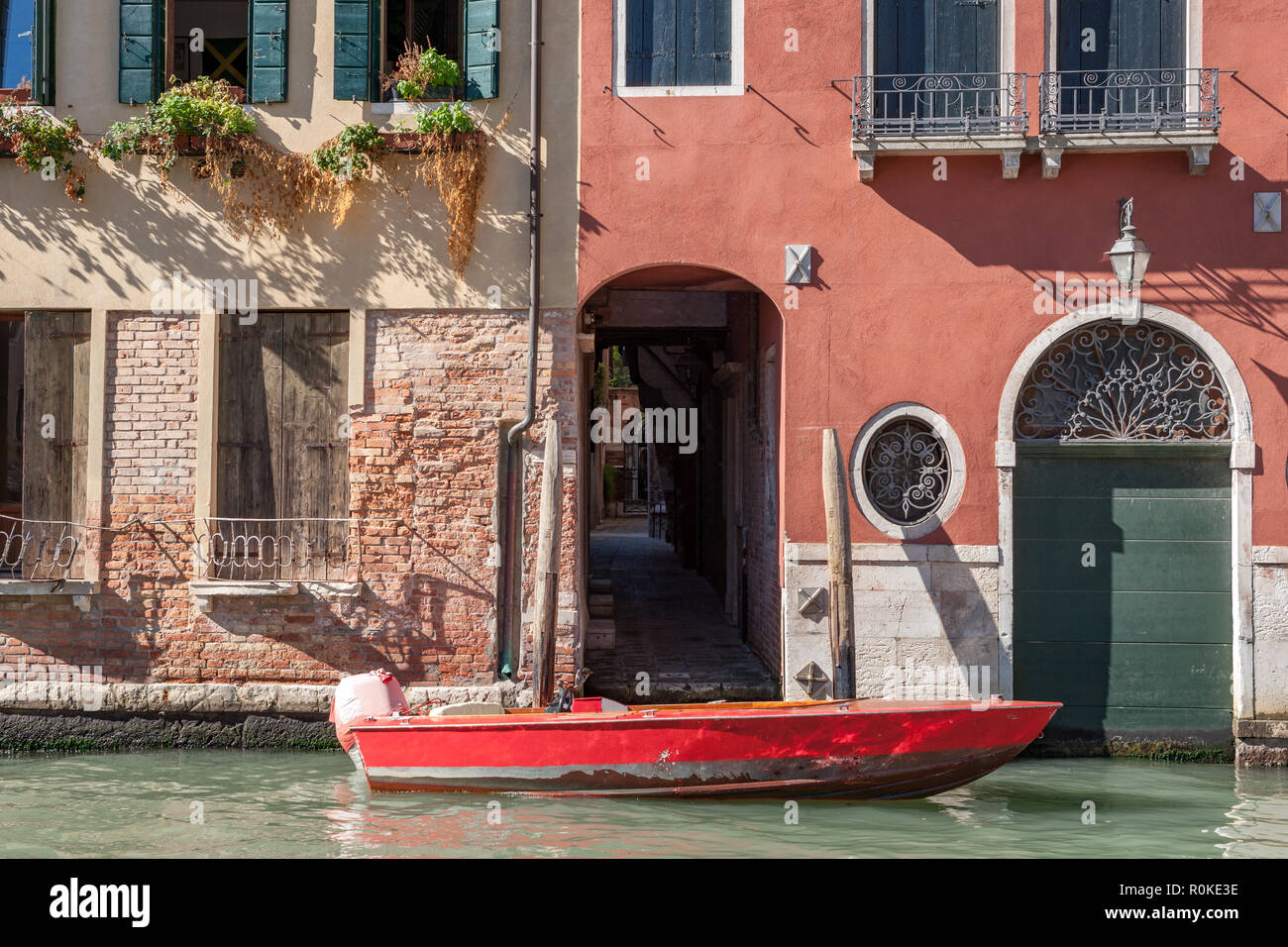 Red wooden boat moored in front of old colourful builings in Venice Italy Stock Photo
