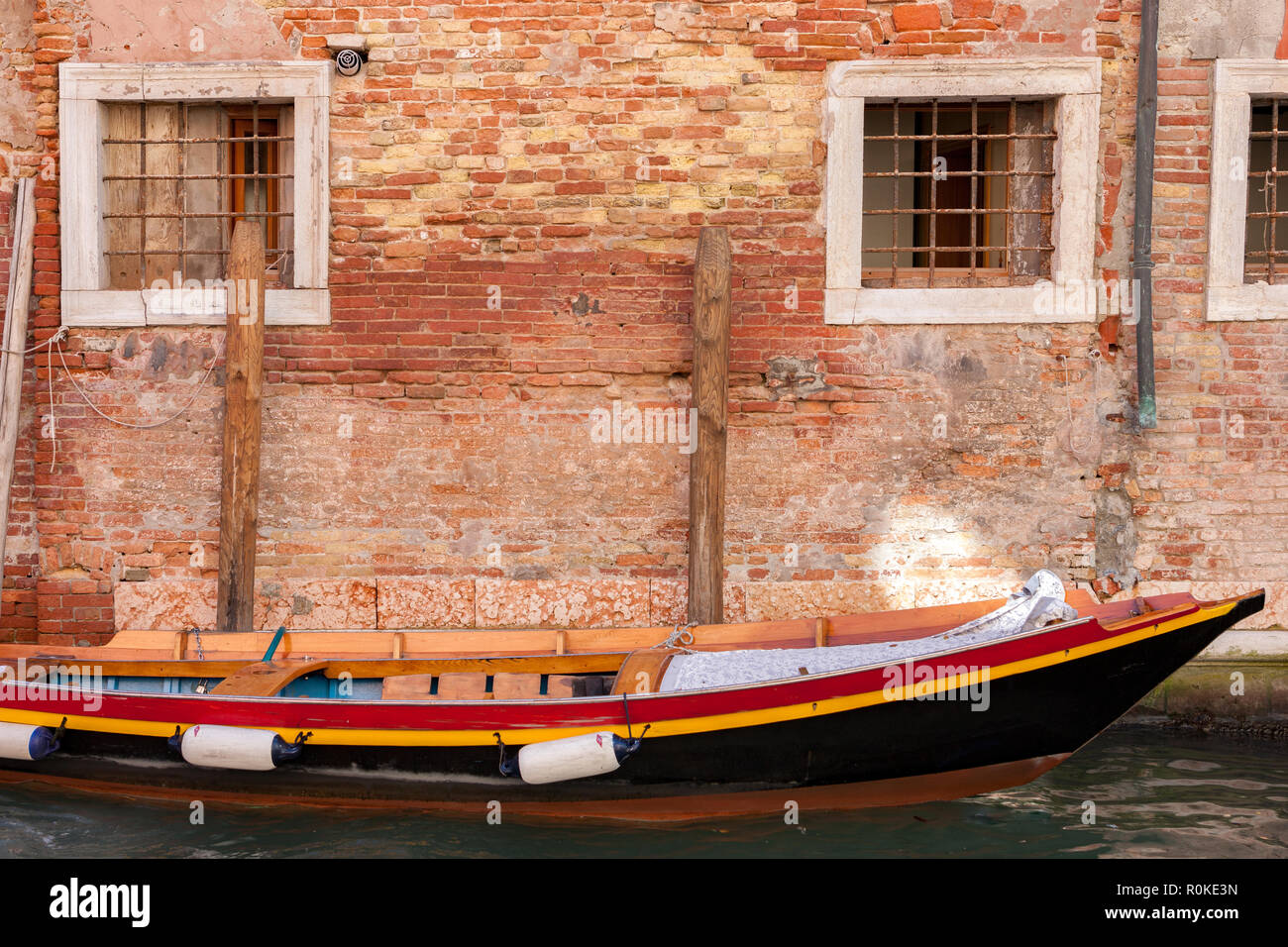 Red wooden boat moored in front of old colourful brick builings in Venice Italy Stock Photo