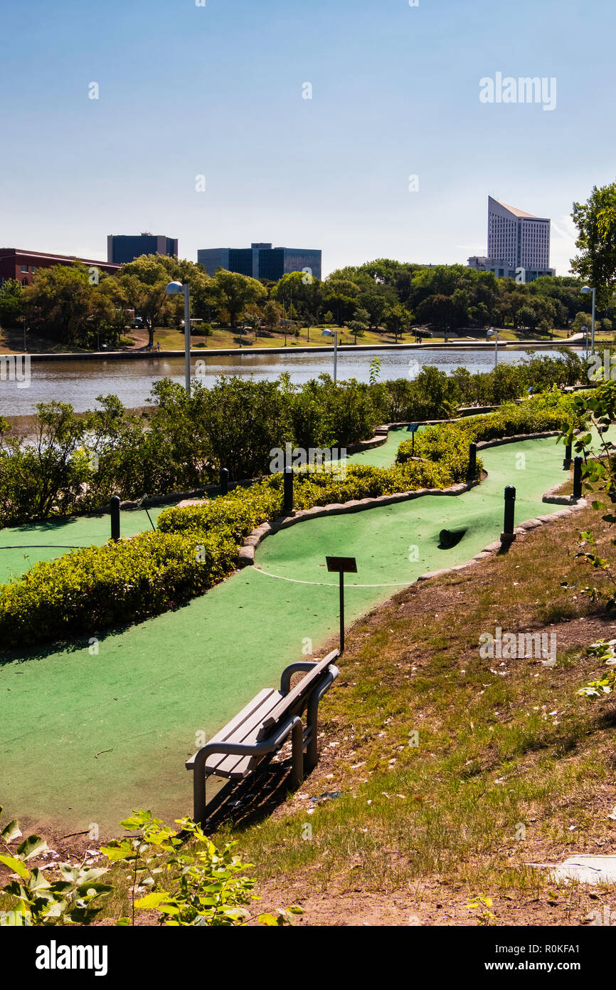 A minature golf course running beside the Arkansas river with city buildings  in background. River Walk on opposite shore. Wichita, Kansas, USA. Stock Photo