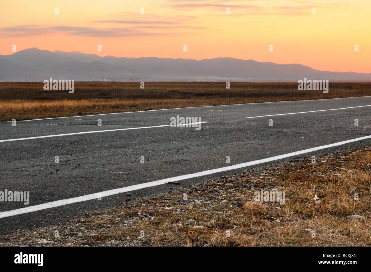 Autumn landscape with an asphalt road and spectacular sunset above mountains on horizon in Khakassia Stock Photo