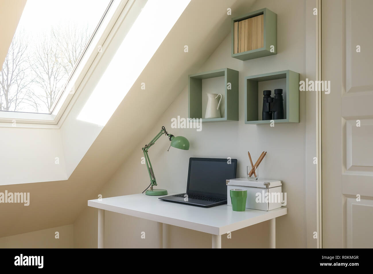 Modern workspace interior. Laptop computer, retro lamp and office accessories on a white desk. Cozy attic / loft apartment with skylight window lettin Stock Photo