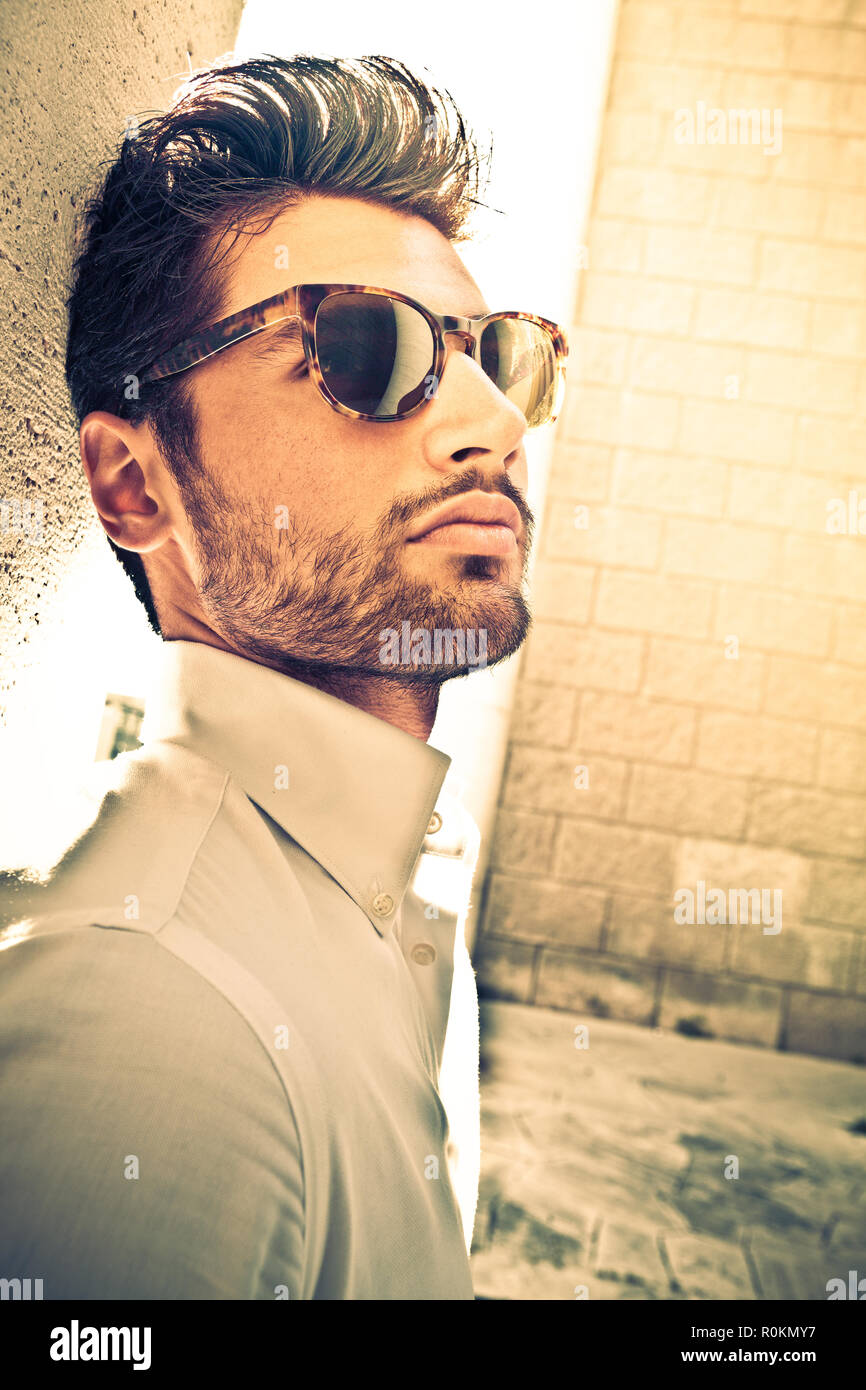 Cool and handsome man with sunglasses outdoor. Leaning to a wall. Soft beard  anche charming and attractive look. White shirt. Intense warm lights Stock  Photo - Alamy