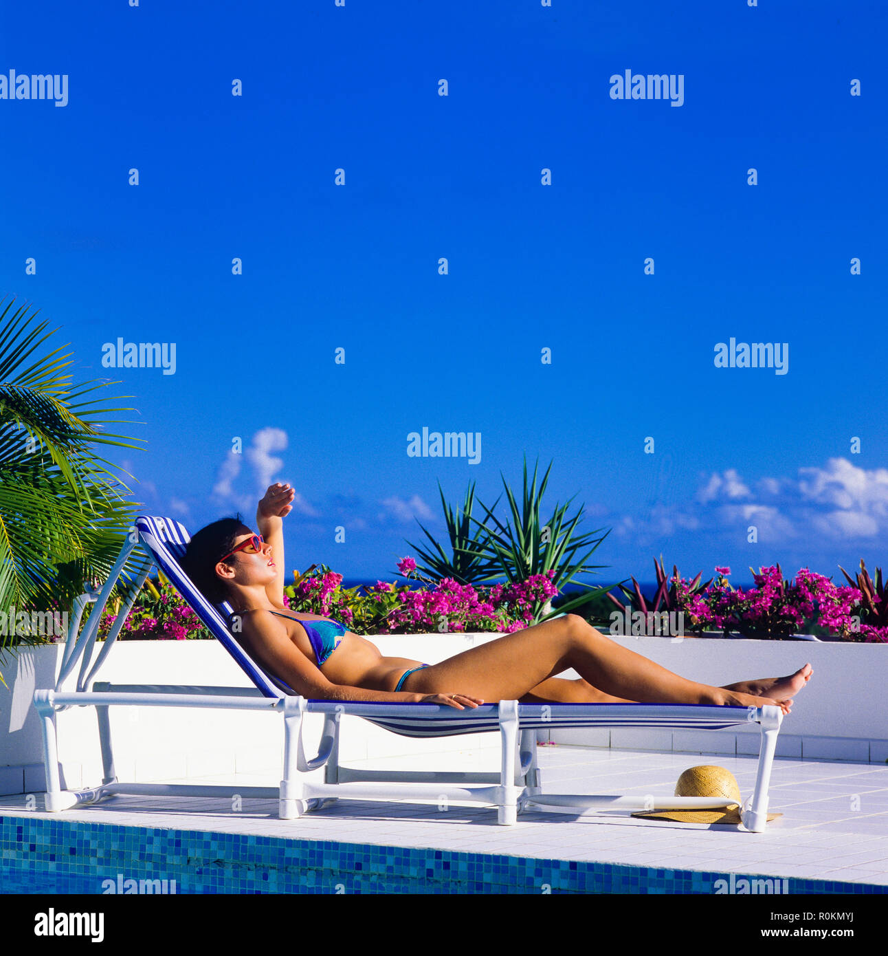 Young woman with blue bikini sunbathing on sun lounger at poolside, Guadeloupe, French West Indies, Stock Photo
