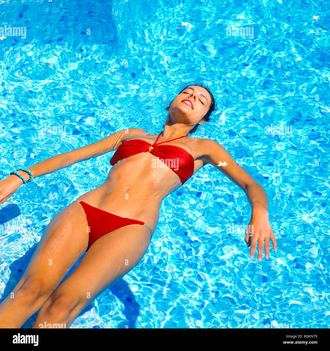 Young woman with red bikini floating on water in swimming pool, Guadeloupe, French West Indies, Stock Photo