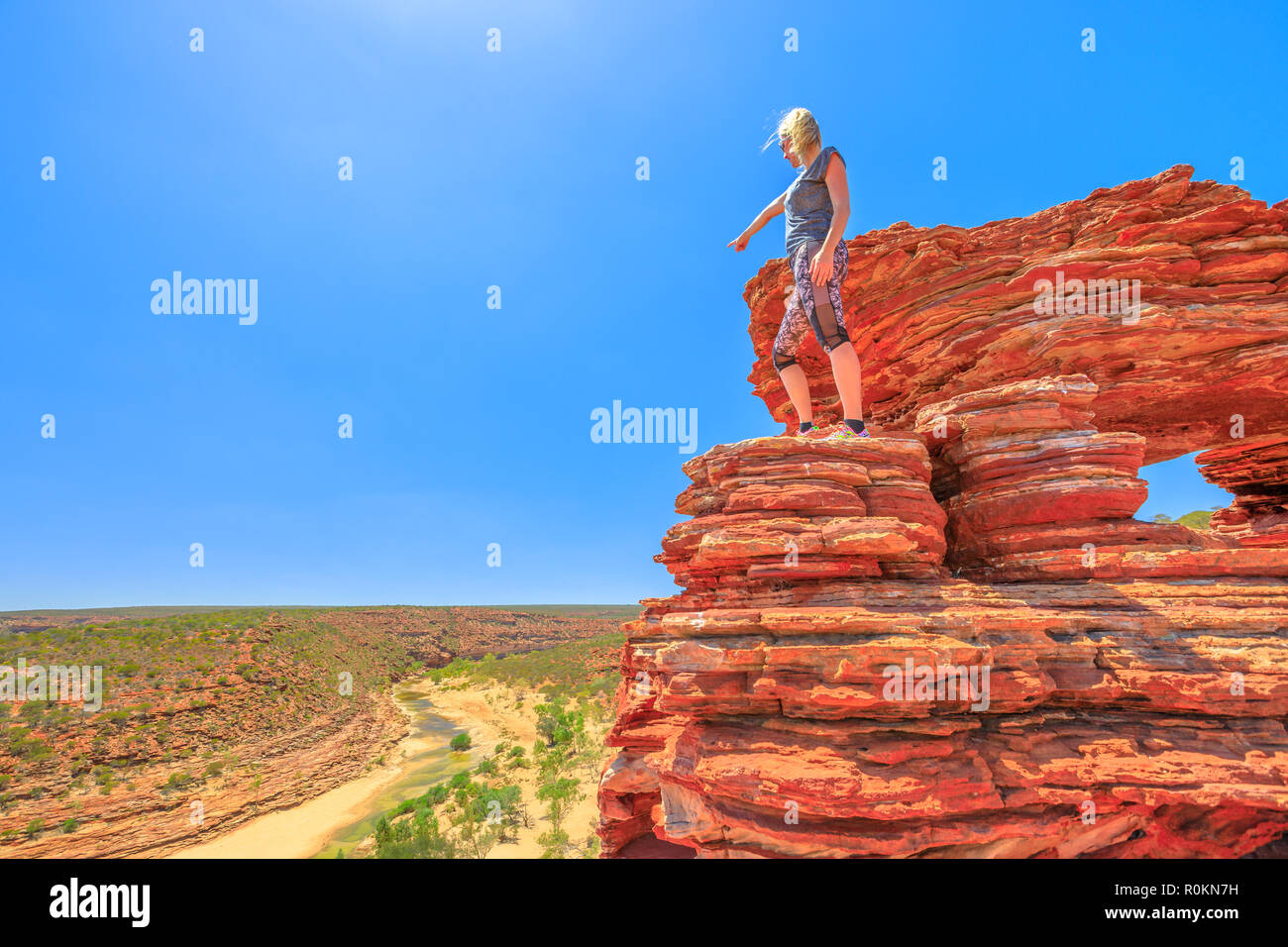 Backpaker woman over iconic Nature's Window, with rocks rippled with red and white banded, pointing Murchison River in Kalbarri National Park, Western Australia. Australia, outback travel. Copy space. Stock Photo