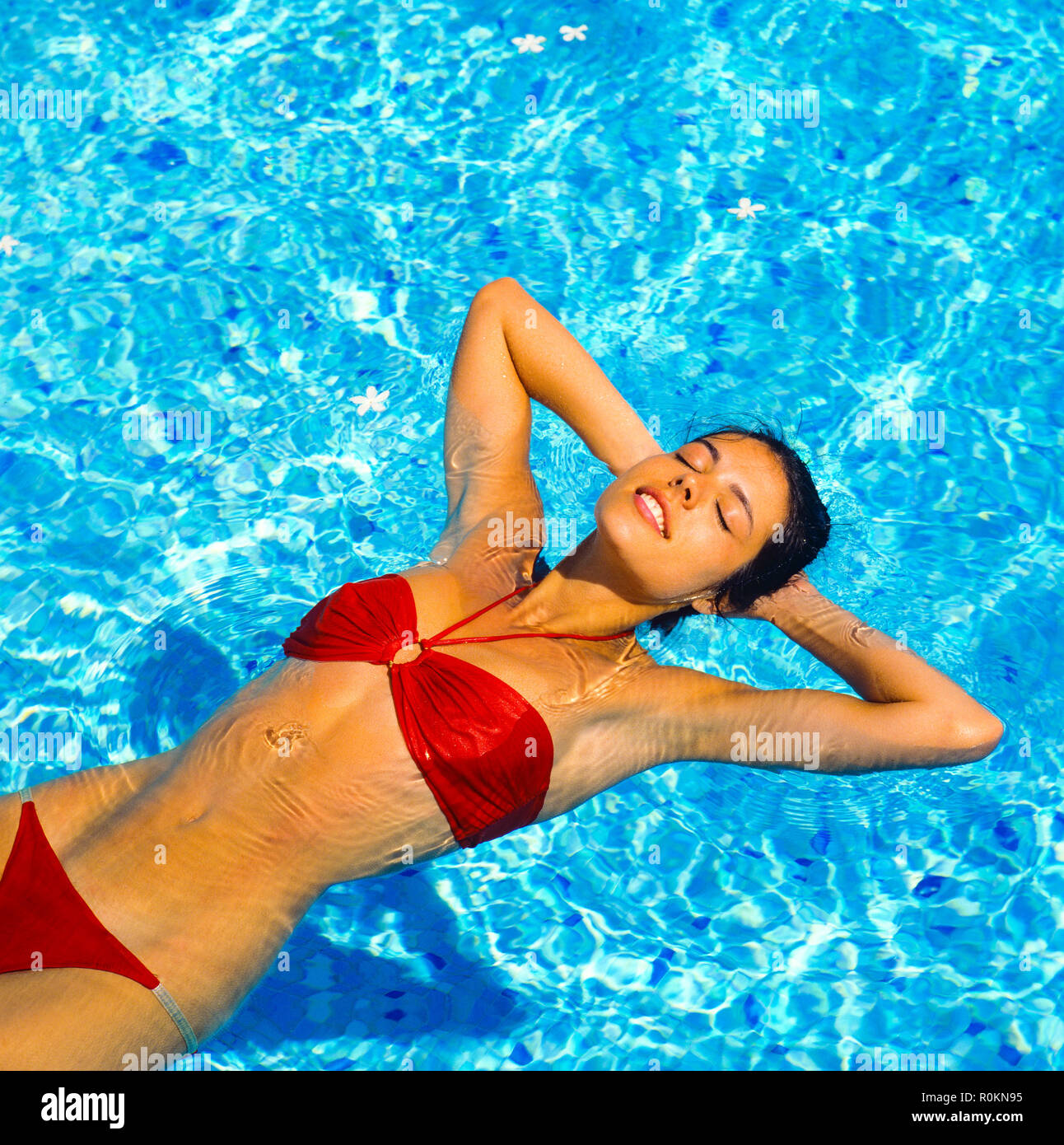 Young woman with red bikini floating on water in swimming pool, Guadeloupe, French West Indies, Stock Photo