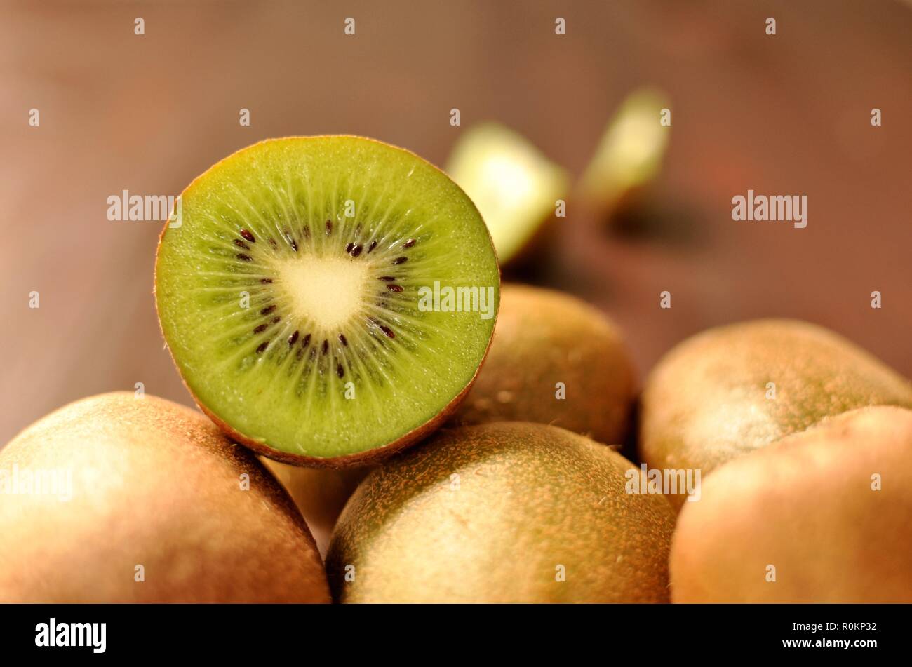 Group of ripe whole kiwi fruit and half kiwi fruit on brown wooden background. Front view, selective focus Stock Photo