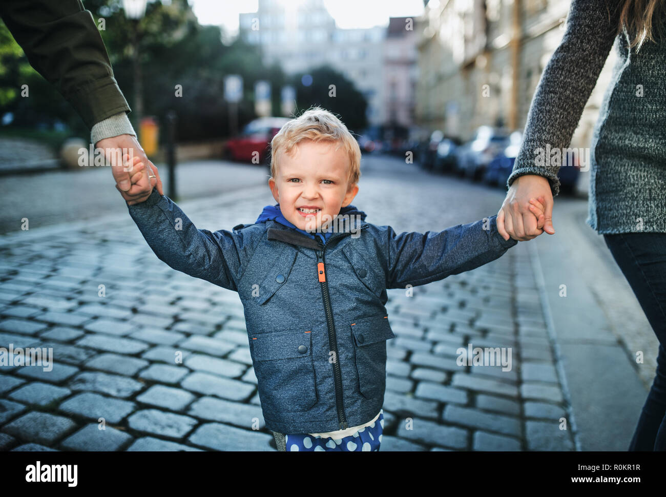 A small toddler boy with unrecognizable parents walking outdoors in city. Stock Photo