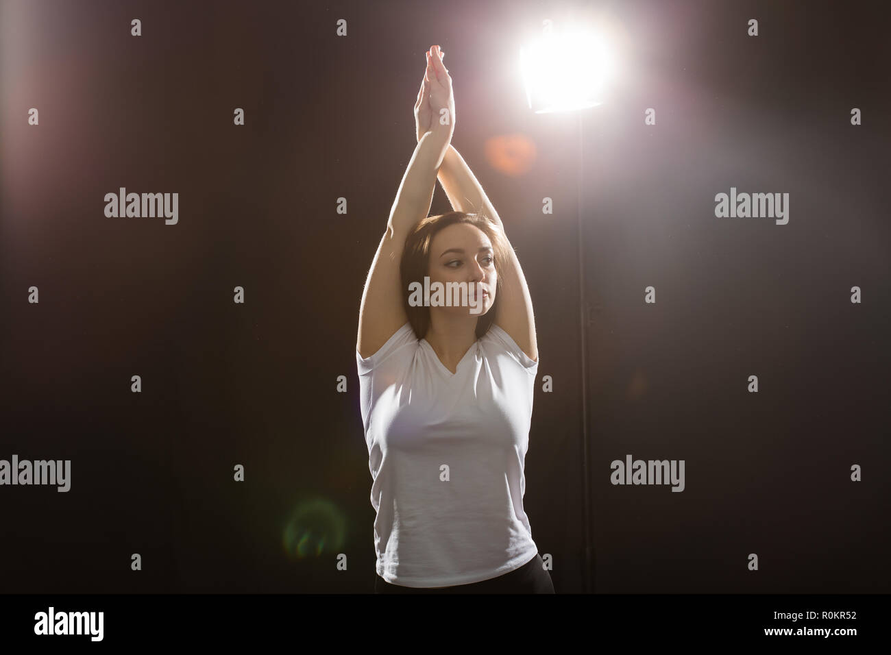 Dancing, jazz-funk and hip-hop concept - young woman dancing in darkness and folded her arms over her head Stock Photo