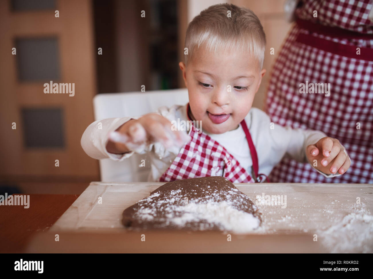 A handicapped down syndrome child with his mother indoors baking. Stock Photo