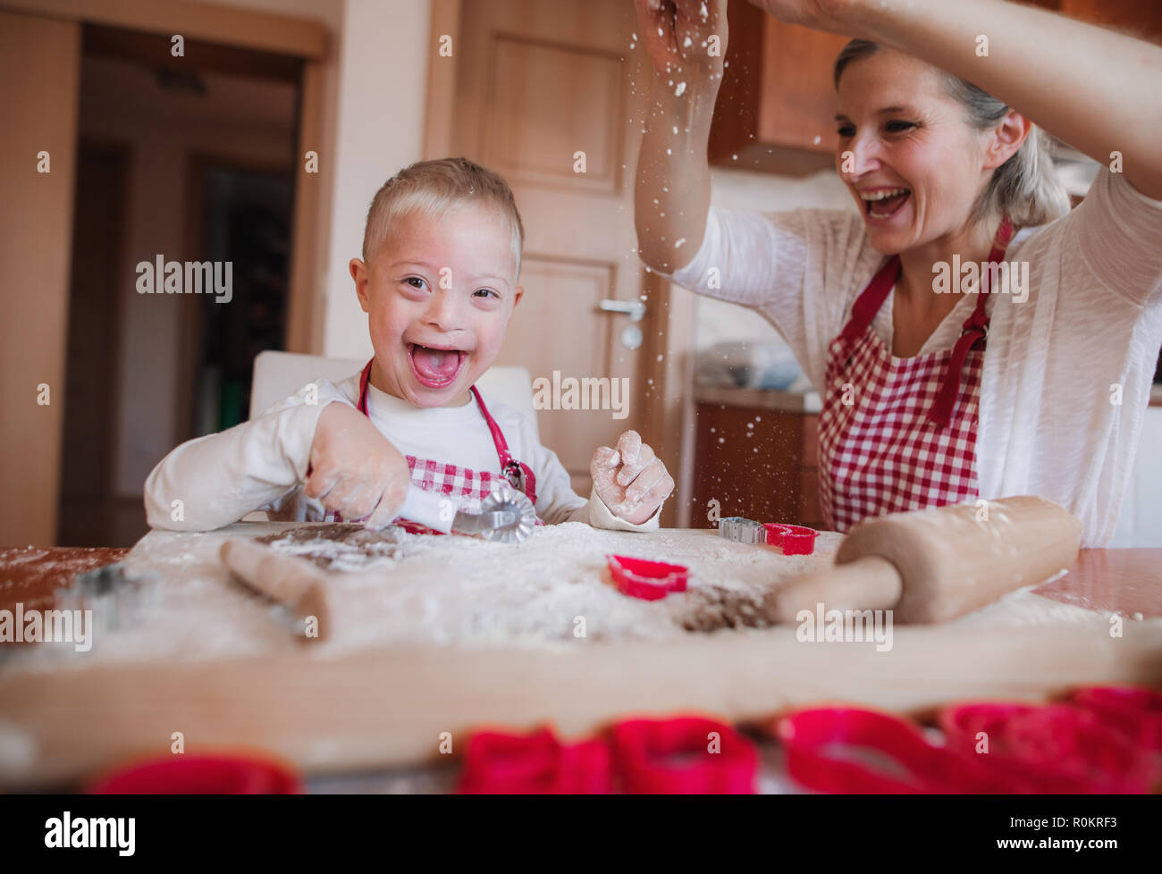 A laughing handicapped down syndrome child with his mother indoors baking. Stock Photo