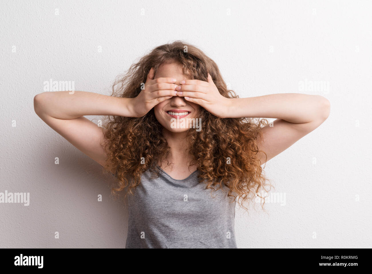 Young beautiful happy woman in studio, covering her eyes. Stock Photo