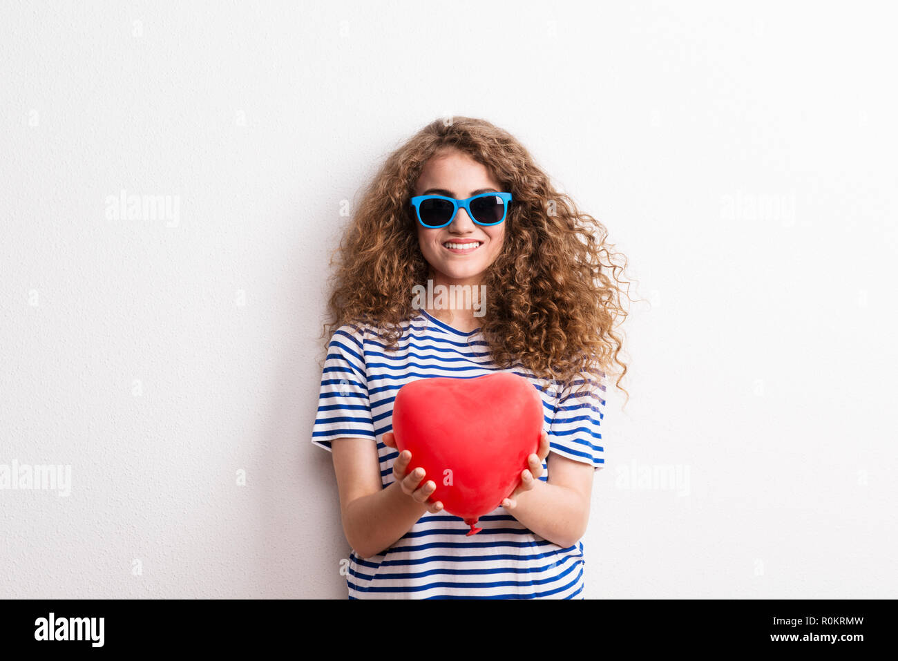 Young beautiful cheerful woman with sunglasses in studio, holding red heart. Stock Photo