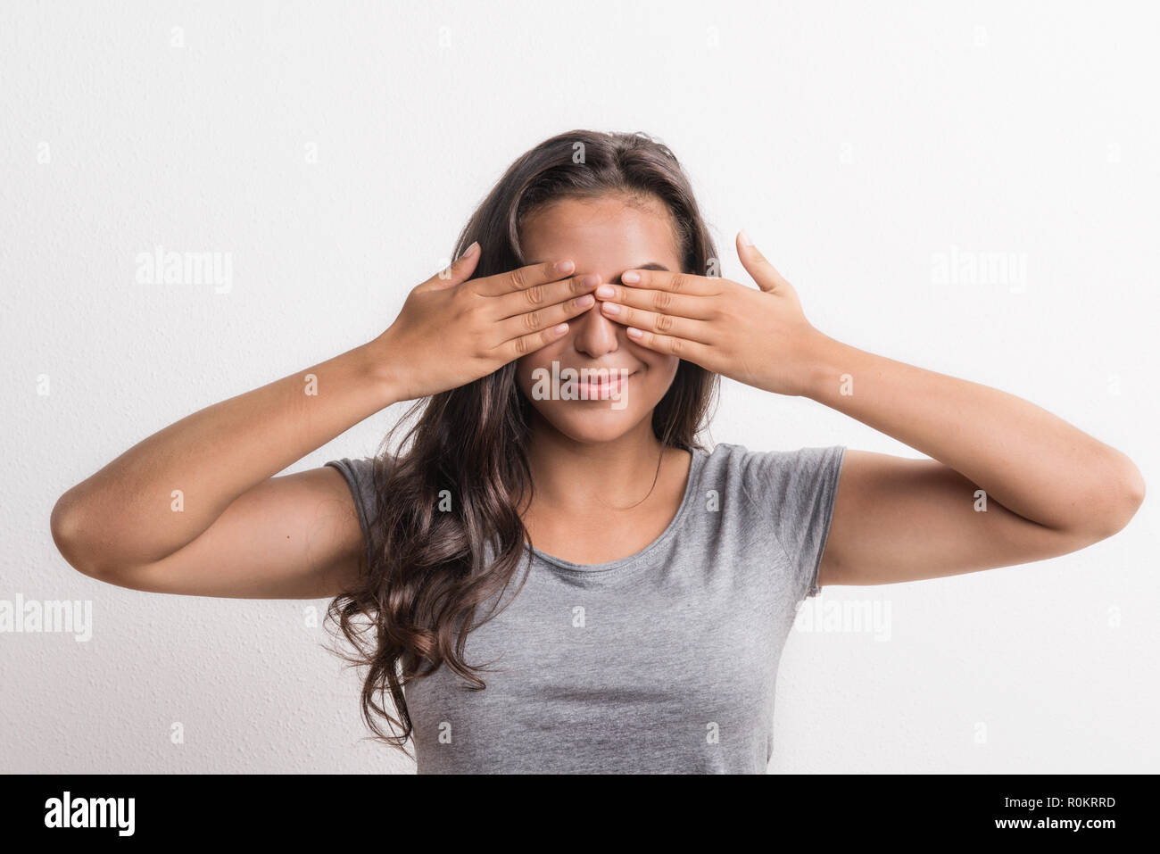 Young beautiful happy woman in studio, covering her eyes. Stock Photo