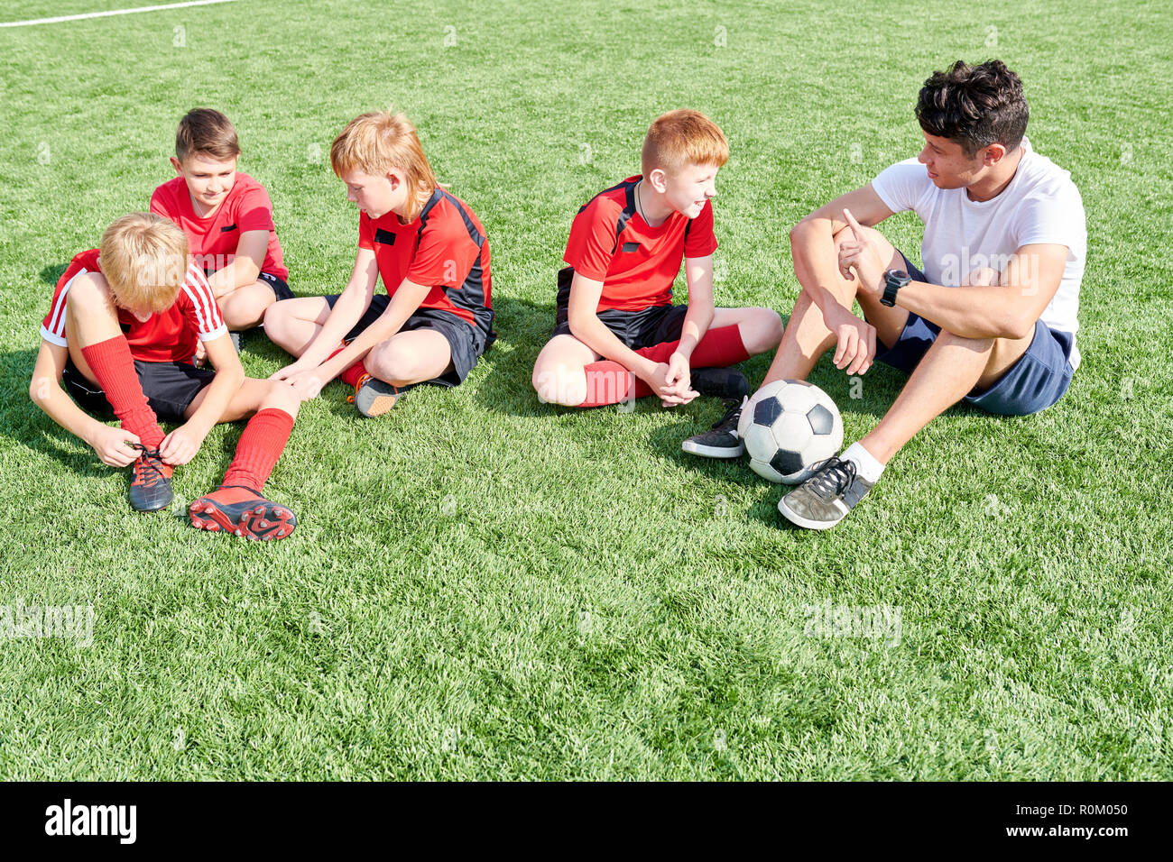 Play in the school football team. Футболист сидит на траве. Юниорки футбол. Команда сидит жердочке. Дети СЛУШАЮТ тренера.