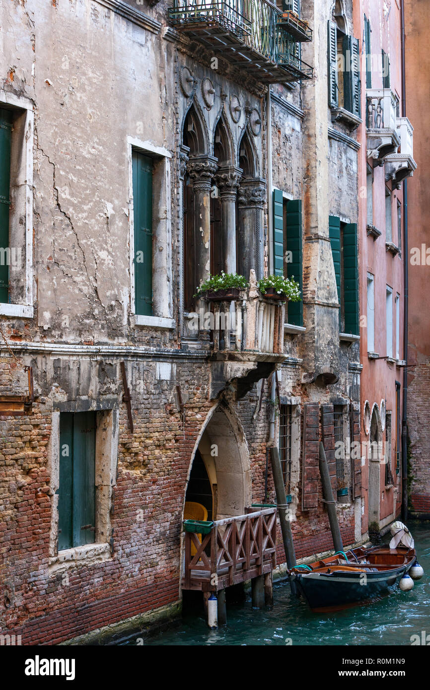 Old brick and painted buildings with balconies and doorways with gondala boats on the canals of Venice Italy Stock Photo