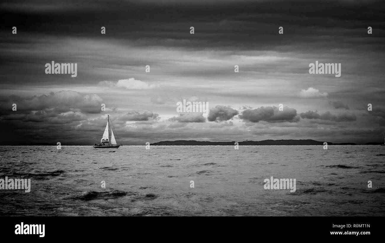 Boat sailing in the upcomming storm. Sailboat in bad weather sail at opened sea. Sailing yacht under heavy cloud sky. Stock Photo