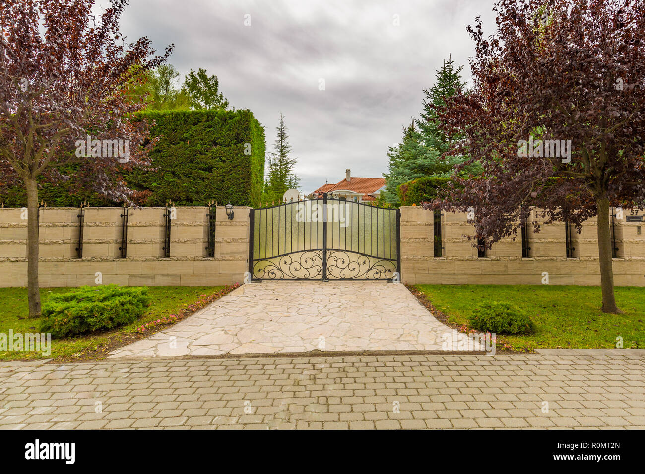Iron gate with trees and stone fence, luxury house or villa guard. Elegant driveway towards