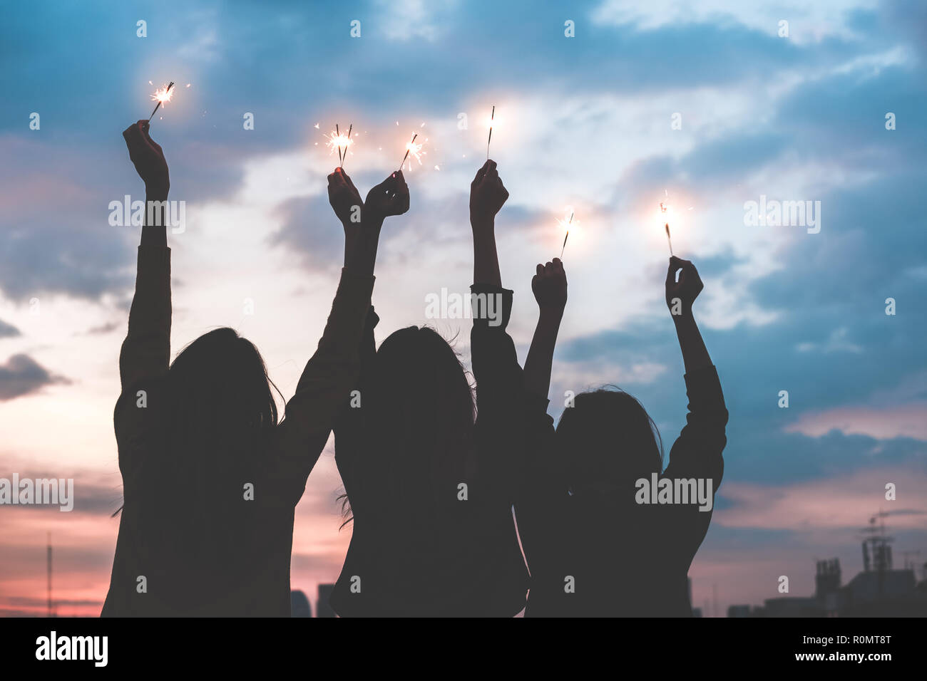 silhouette happy group of asia girl friends enjoy and play sparkler at rooftop party at evening sunset,Holiday celebration festive,teeage lifestyle,fr Stock Photo