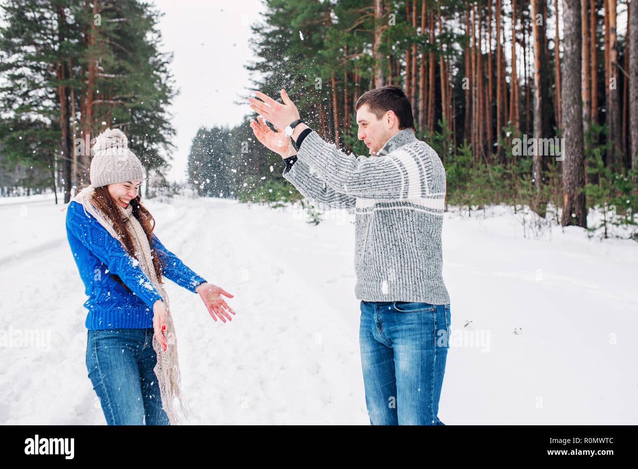 Snowball fight. Winter couple having fun playing in snow forest. Young joyful happy multi-racial couple. Stock Photo