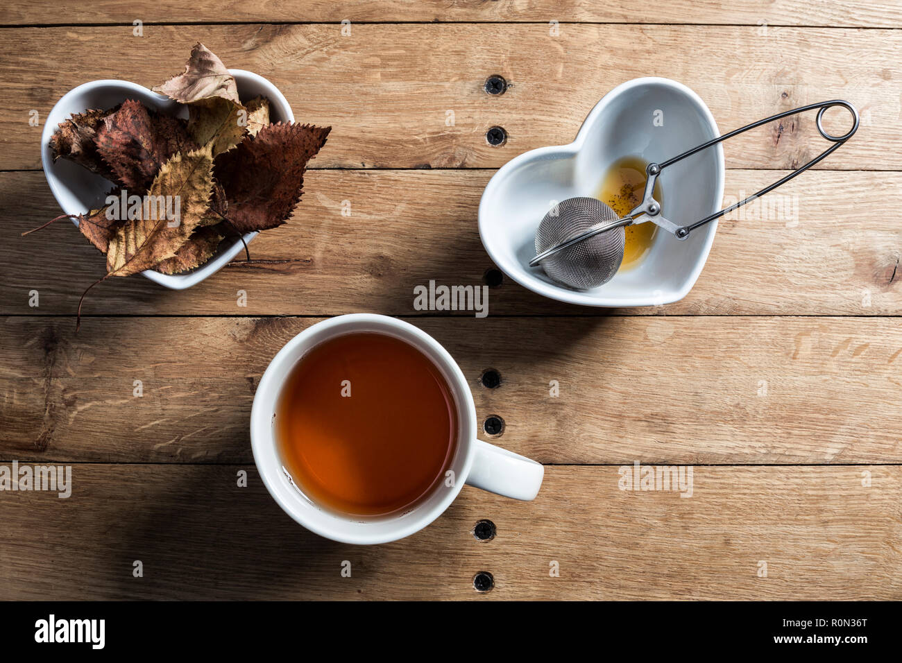 A mug of herbal tea with a steel mesh strainer and autumn leaves table decoration. Stock Photo