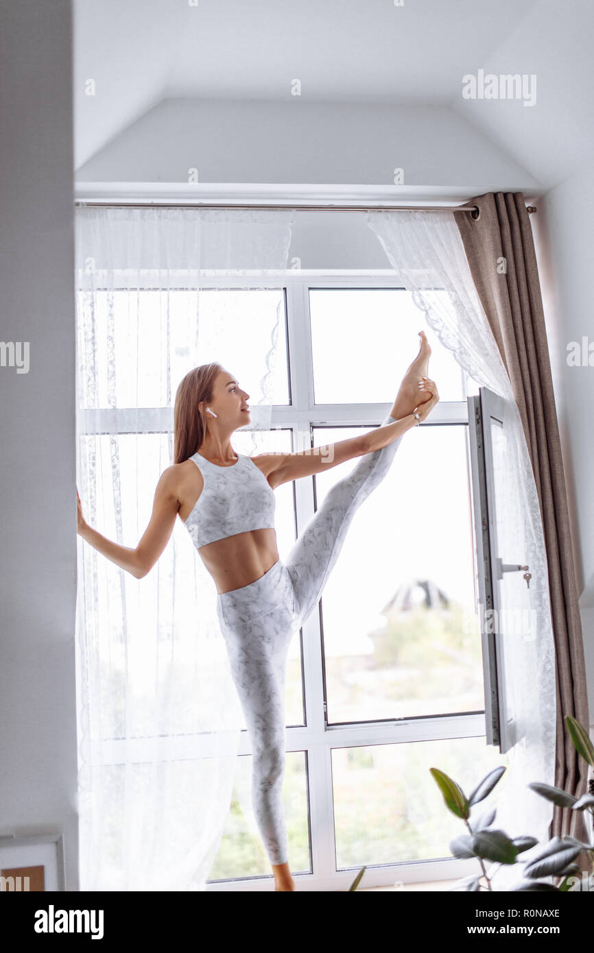 Young skinny flexiable woman doing yoga on one leg against window vertical  split Stock Photo - Alamy