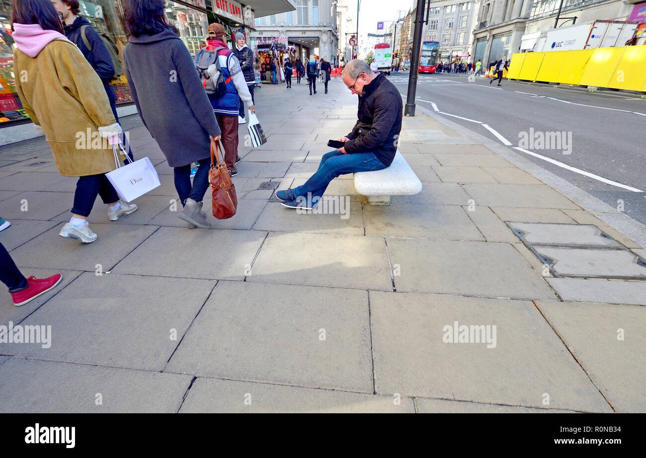 Man sitting on a seat in Oxford Street with his mobile phone, London, England, UK. Stock Photo