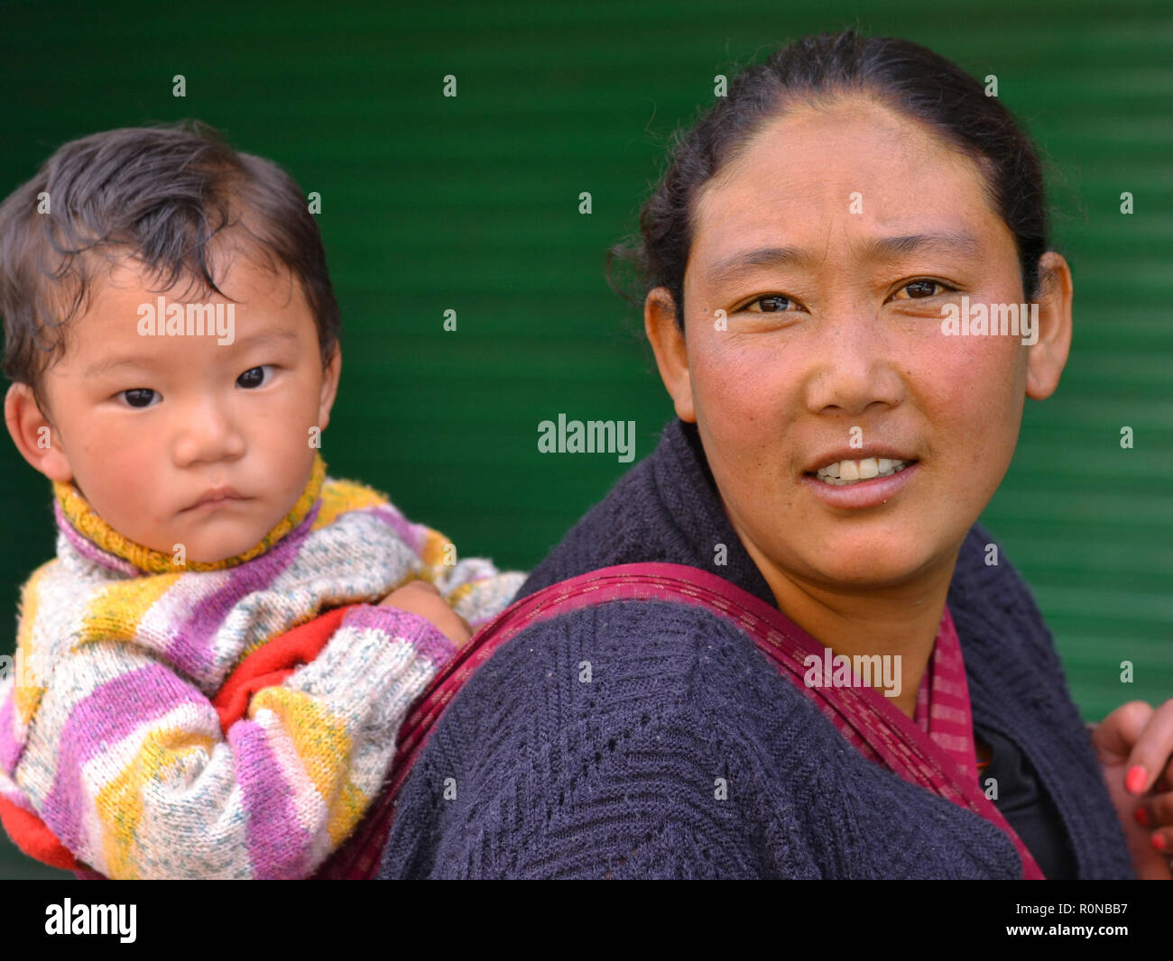 Young Indian Monpa hill-tribe woman carries her toddler boy in a traditional baby sling on her back. Stock Photo