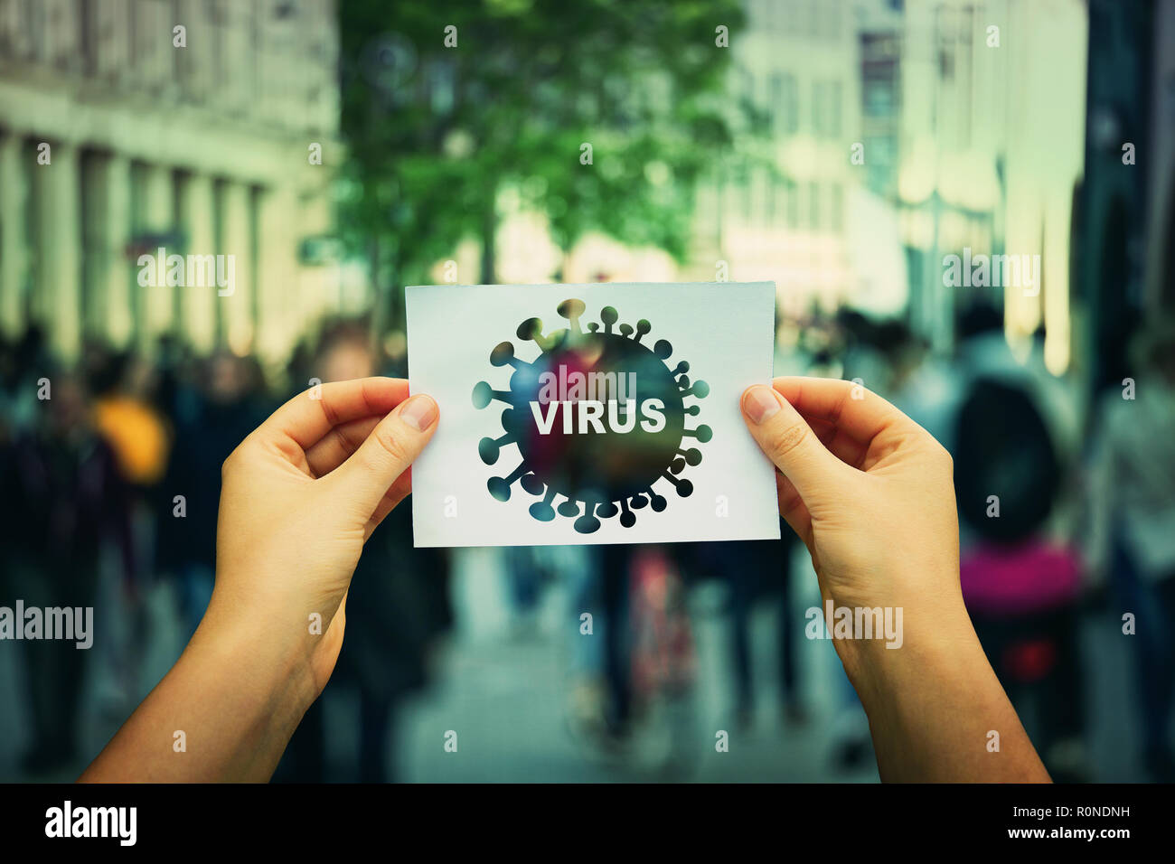 Hands holding a paper sheet with influenza unknown virus spread between human over a crowded city street background. Flu symptoms of fever infecting n Stock Photo
