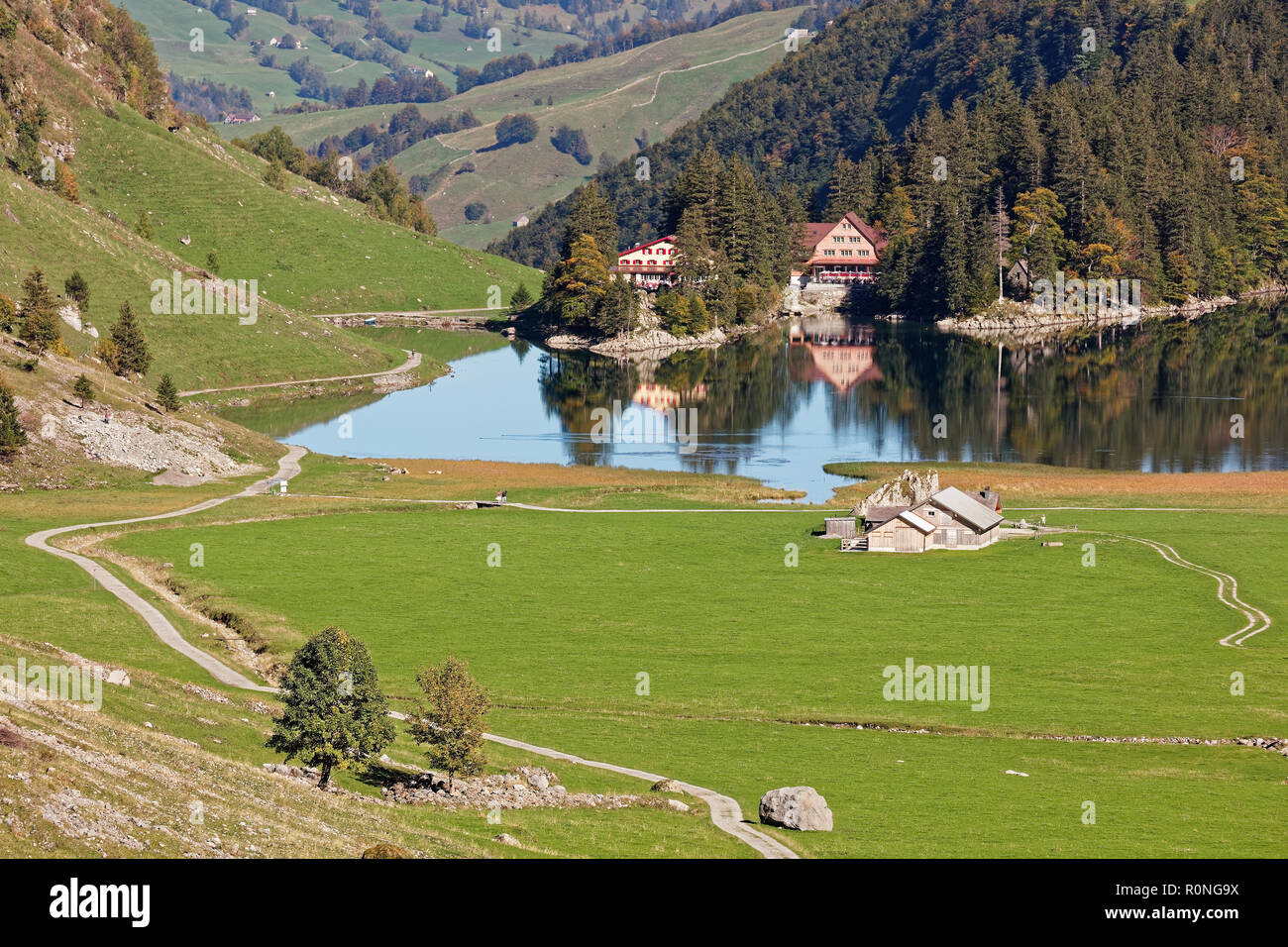 Sunny views of pastures, Seealpsee Inn, Forelle Inn from Oberstofel by Seealpsee lake in Alpstein, Appenzell Alps, Switzerland Stock Photo
