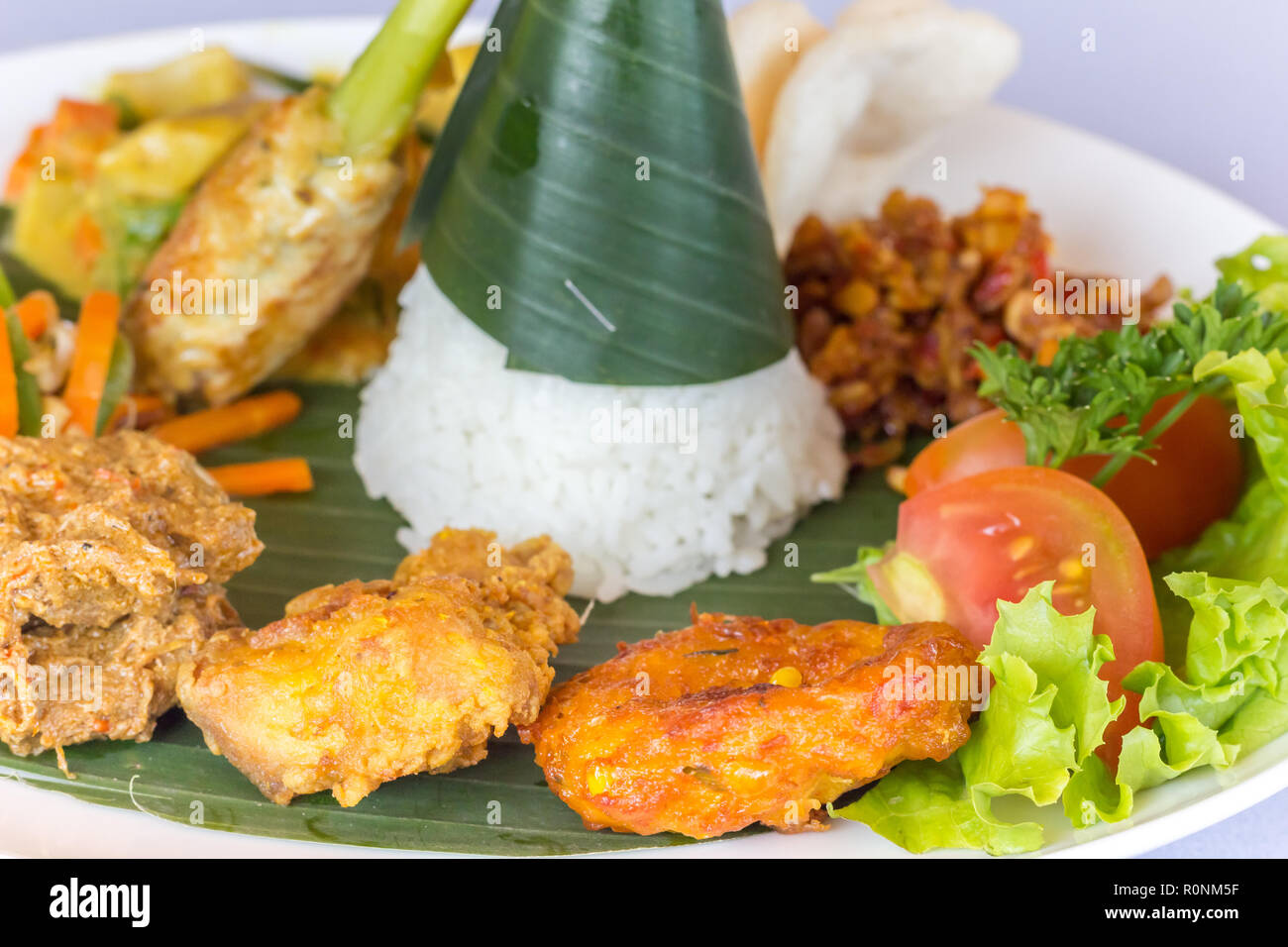 Nasi Campur Bali with tempeh, chicken and vegetables, served on a banana leaf Stock Photo