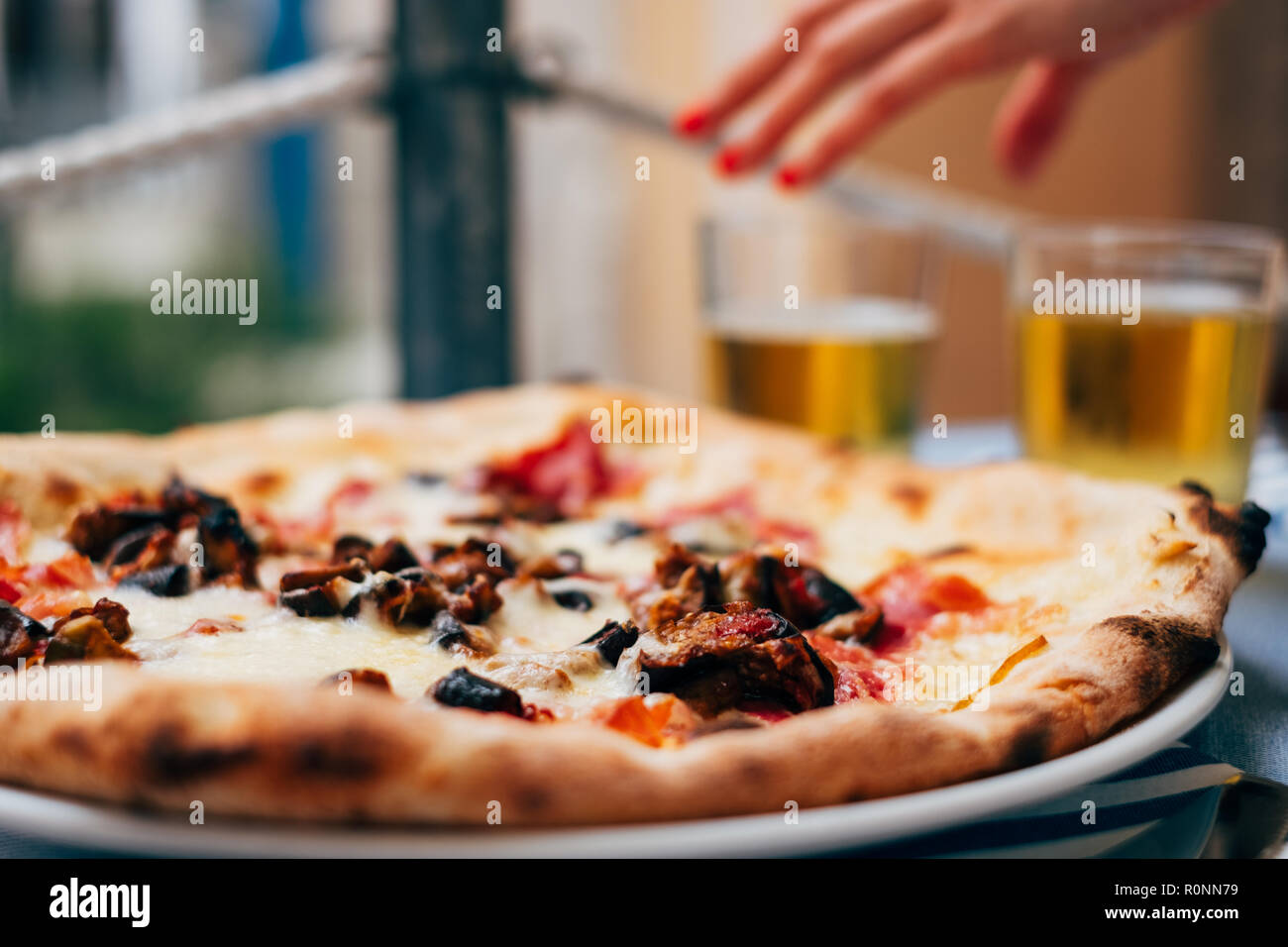 Aubergine pizza on a table and a woman's hand reaching for a beer Stock Photo