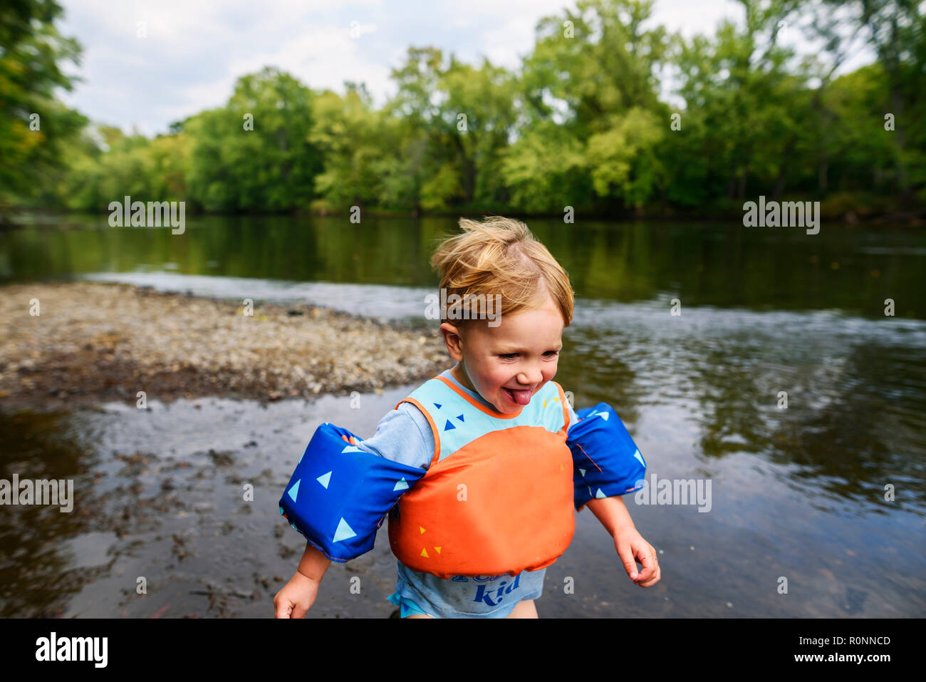 Smiling boy wearing a life jacket running along a riverbank, United States Stock Photo