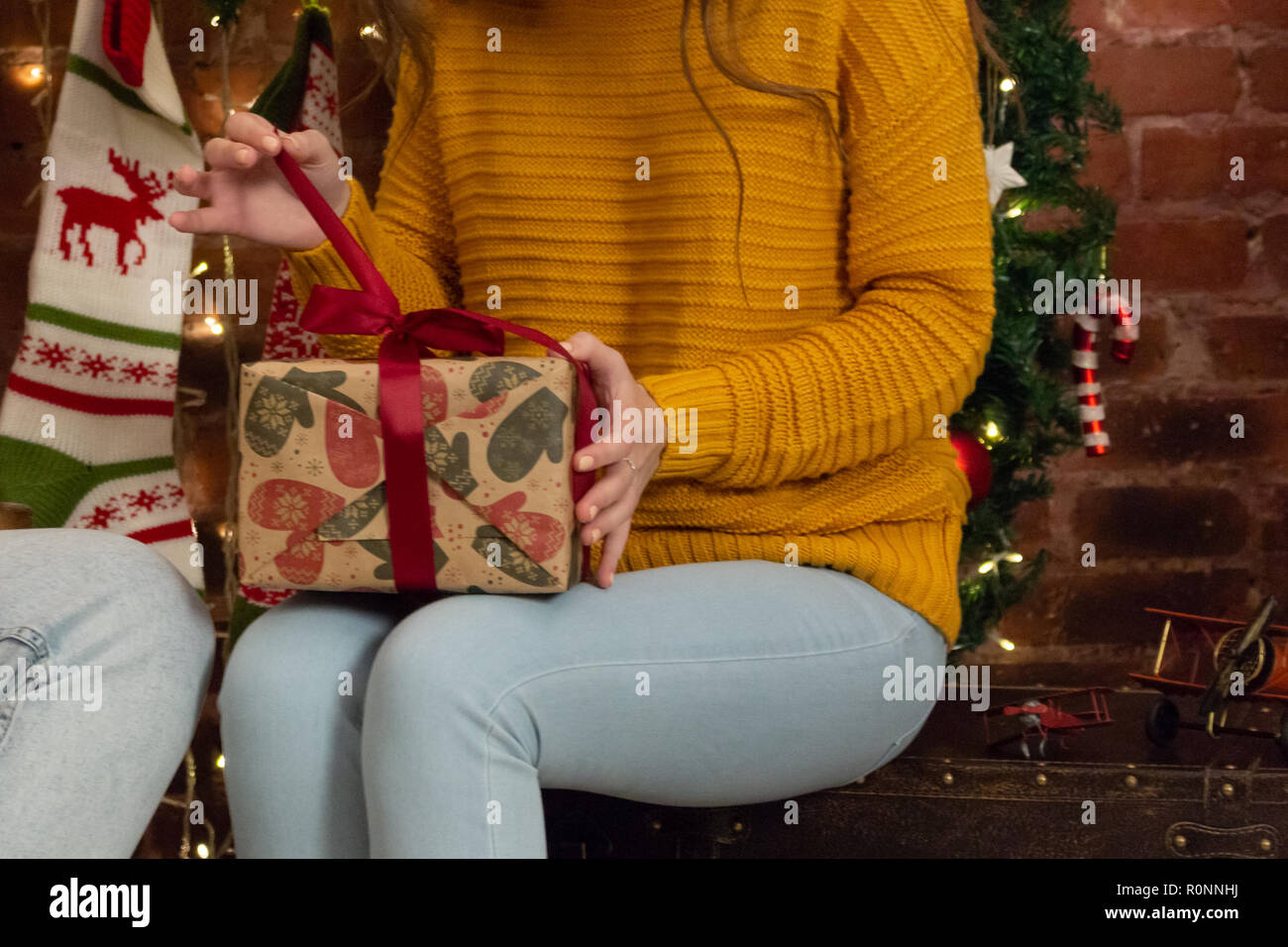 The girl in a yellow sweater unwraps a Christmas gift Stock Photo