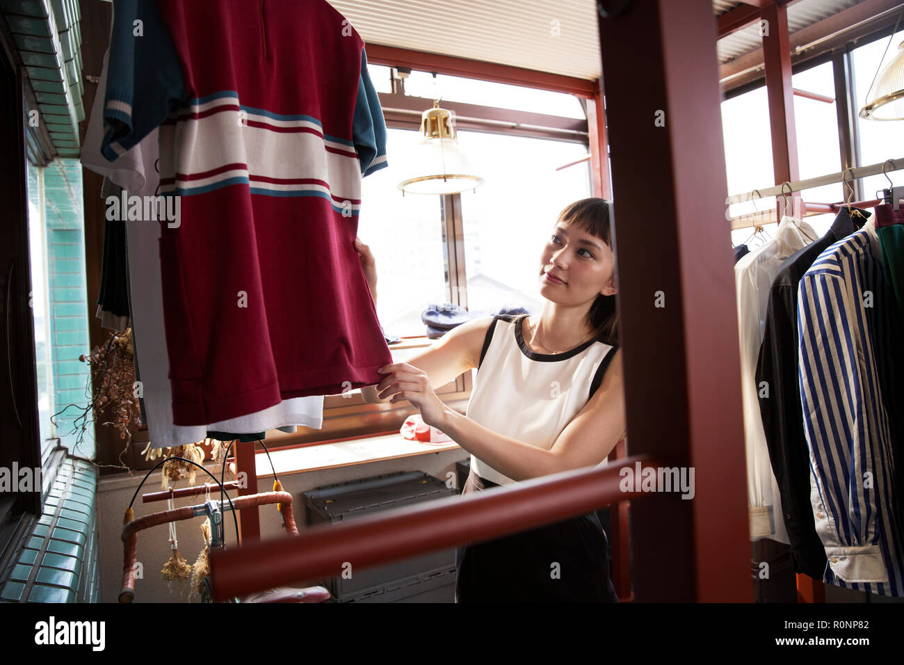 Smiling Japanese saleswoman standing in clothing store, looking at shirt. Stock Photo