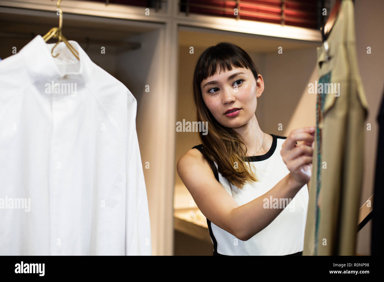 Japanese saleswoman standing in clothing store, looking at shirt. Stock Photo