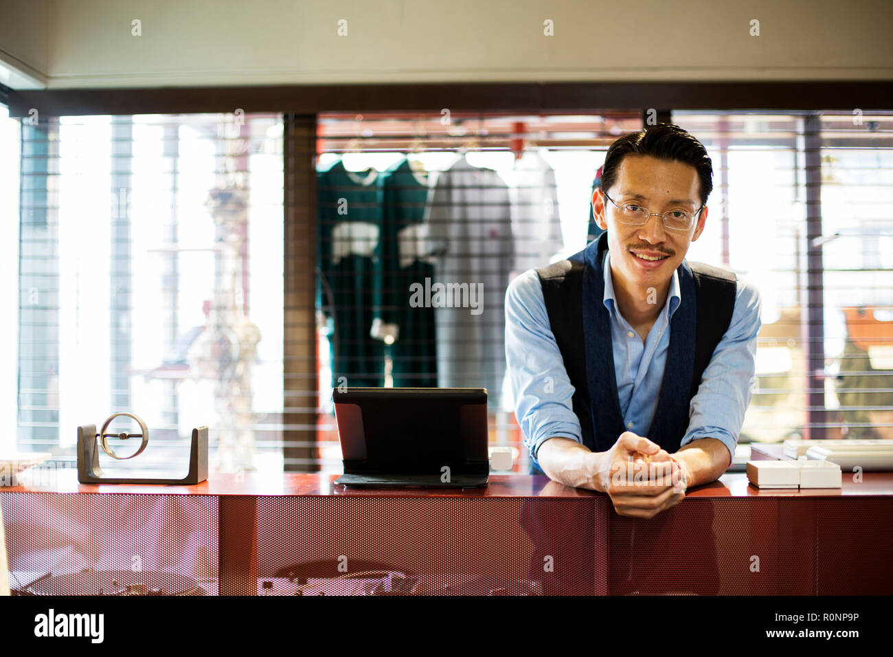 Japanese salesman with moustache wearing glasses standing at counter in