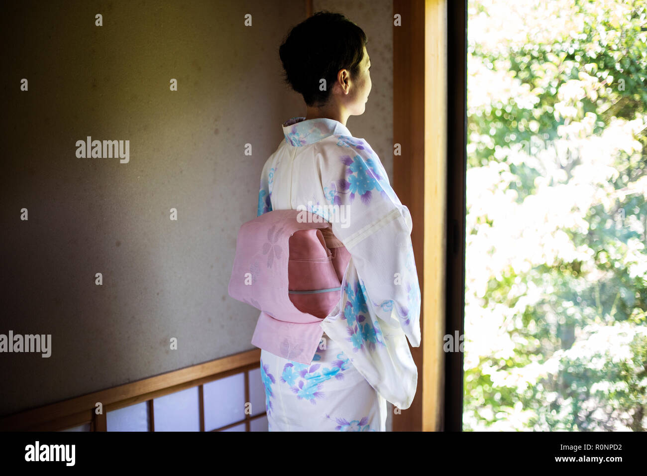 Rear view of Japanese woman standing at window, wearing traditional