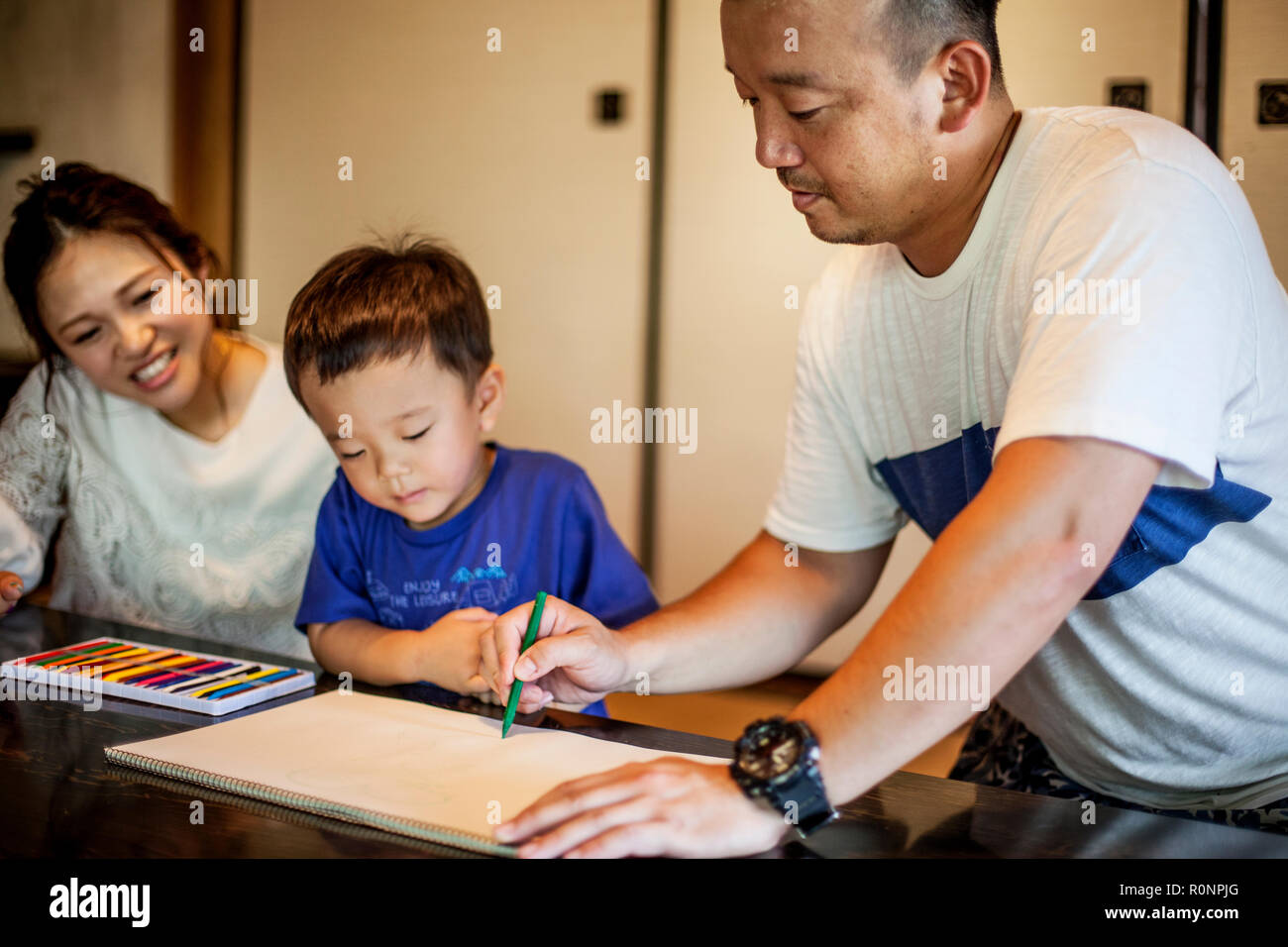Japanese woman, man and little boy sitting at a table, drawing with colouring pens. Stock Photo